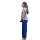 Person wearing a blue floral Papa V Neck top and blue pants standing against a plain wall.