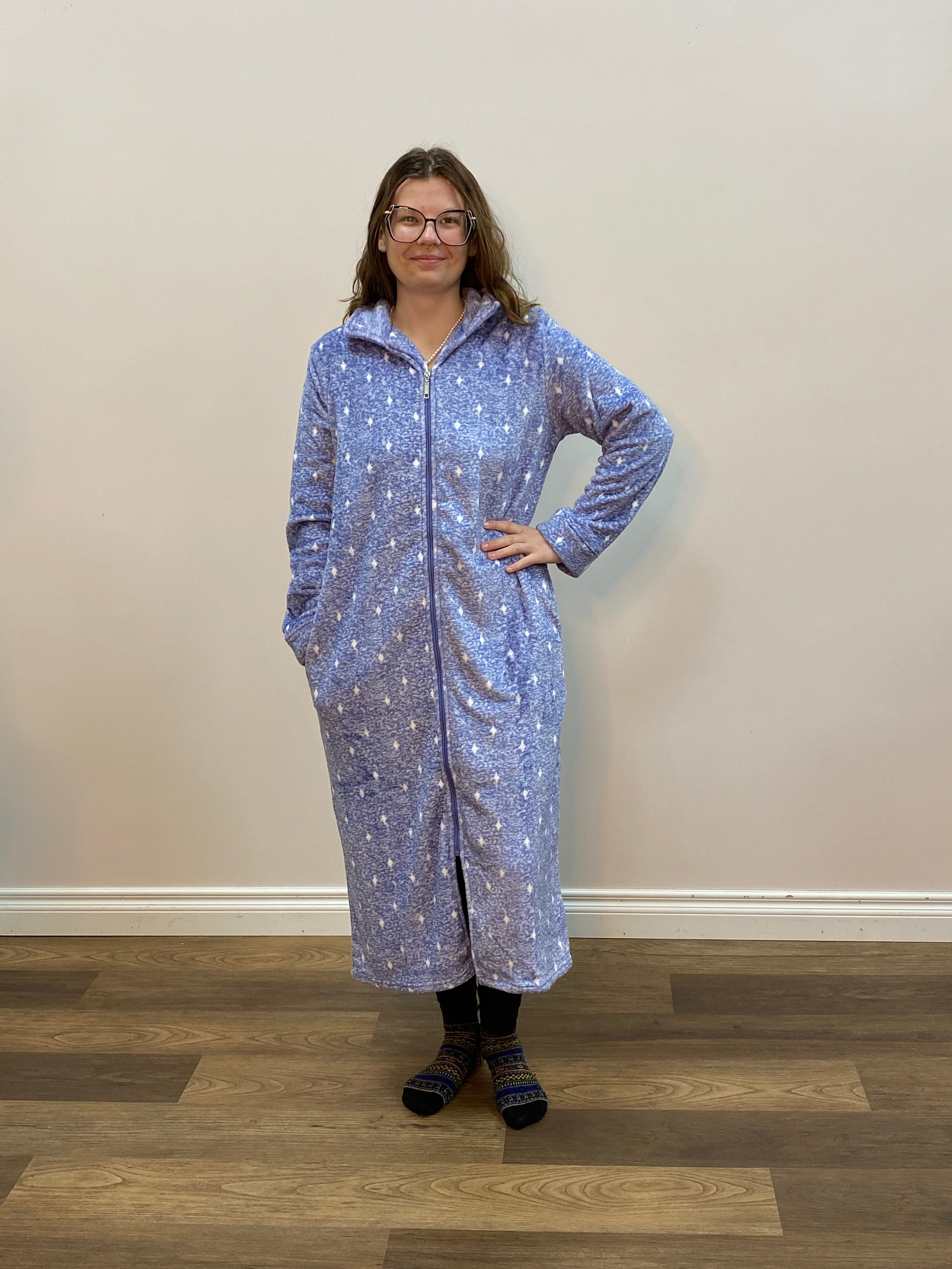 Person wearing a blue patterned robe standing in a room with wooden flooring.