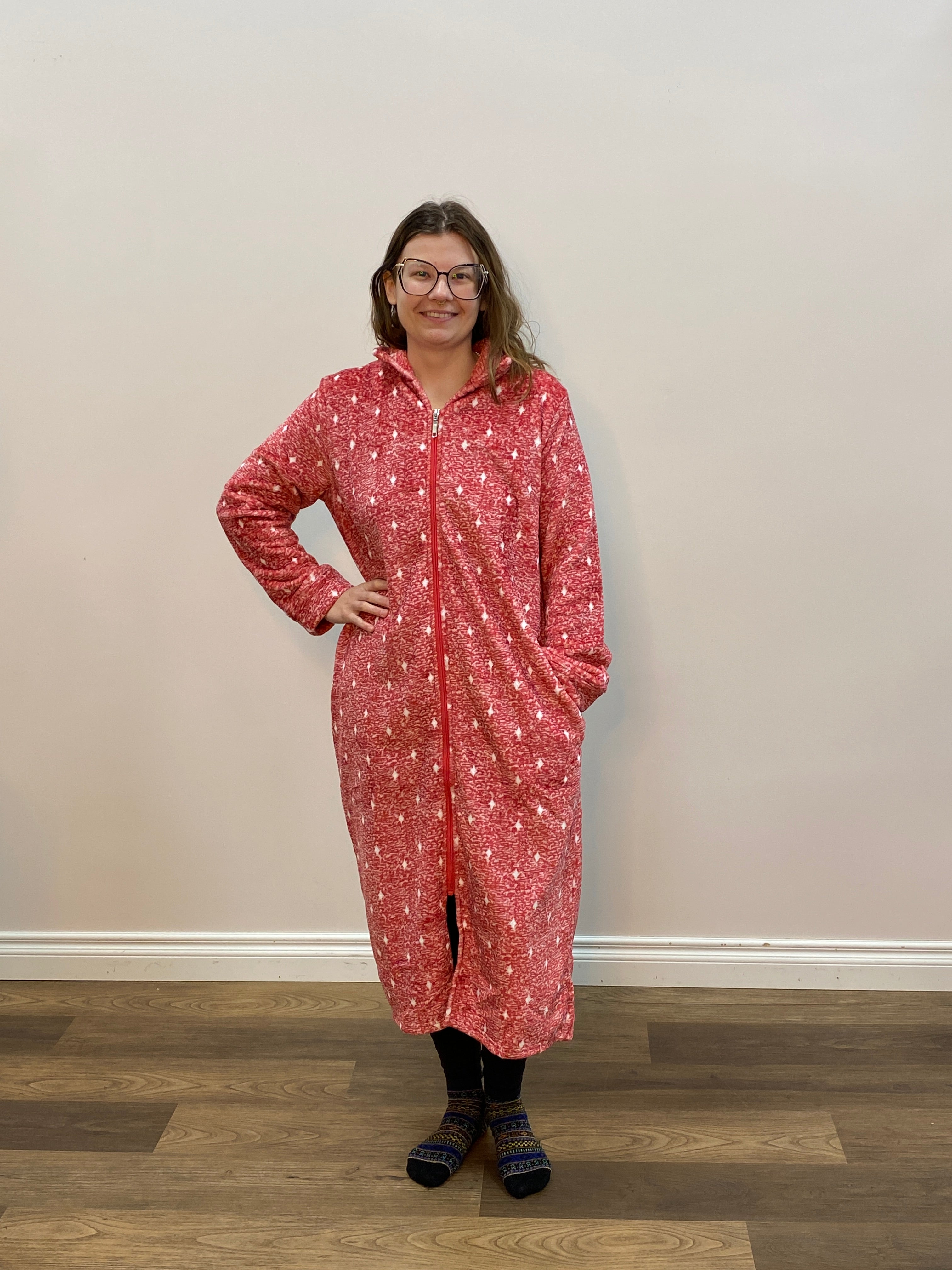 Person wearing a red patterned robe standing in a room with a white wall and wooden floor.