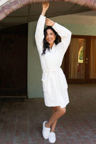 Woman in a white robe standing under an archway with a blurred background