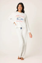 Woman wearing a white long-sleeve top and pants with a graphic design on a plain background