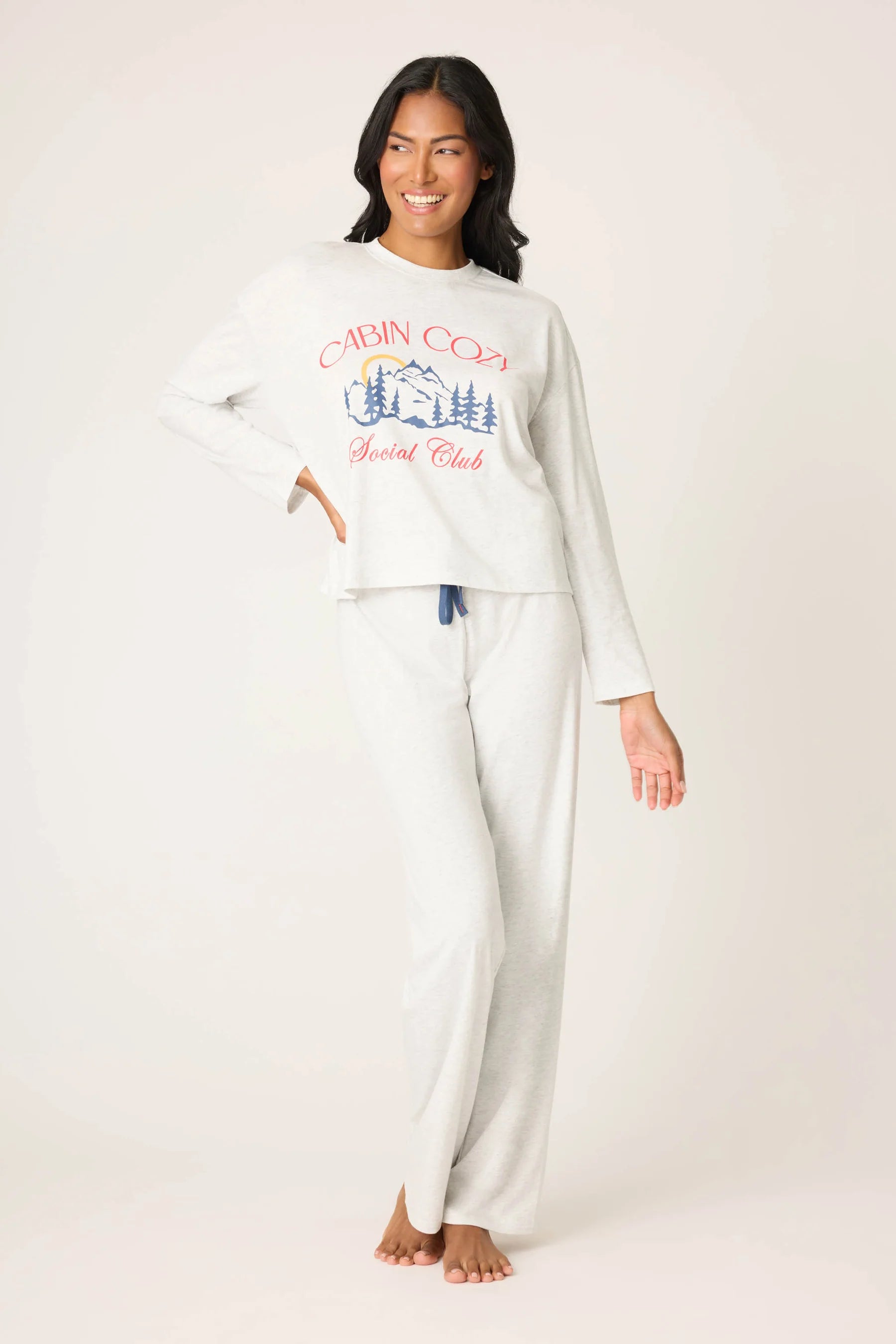Woman wearing a white long-sleeve top and pants with a graphic design on a plain background