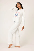 Woman wearing a white sweatshirt with colorful text and matching pants on a plain background