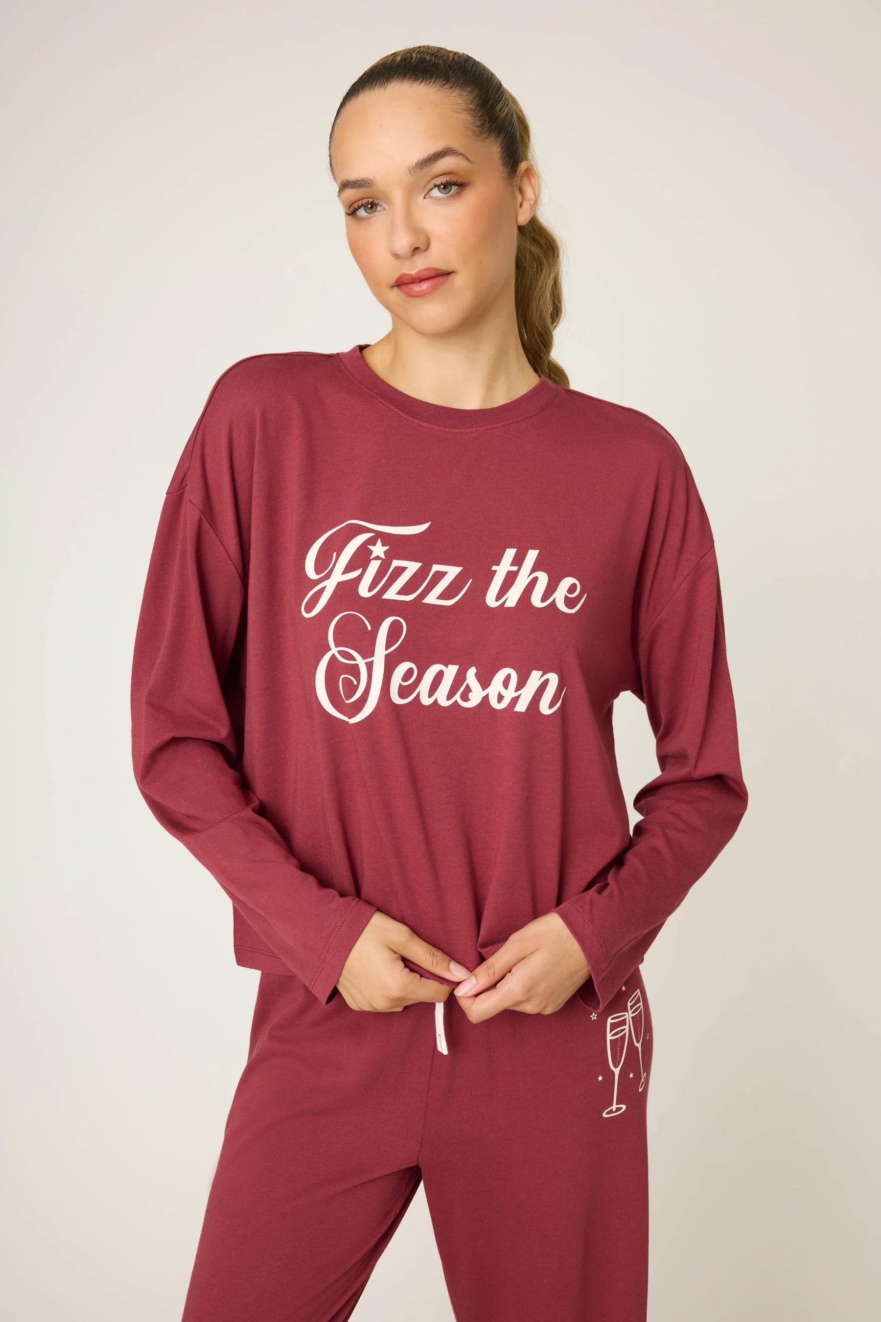 Woman wearing a maroon loungewear set with 'Fizz the Season' text on a plain background