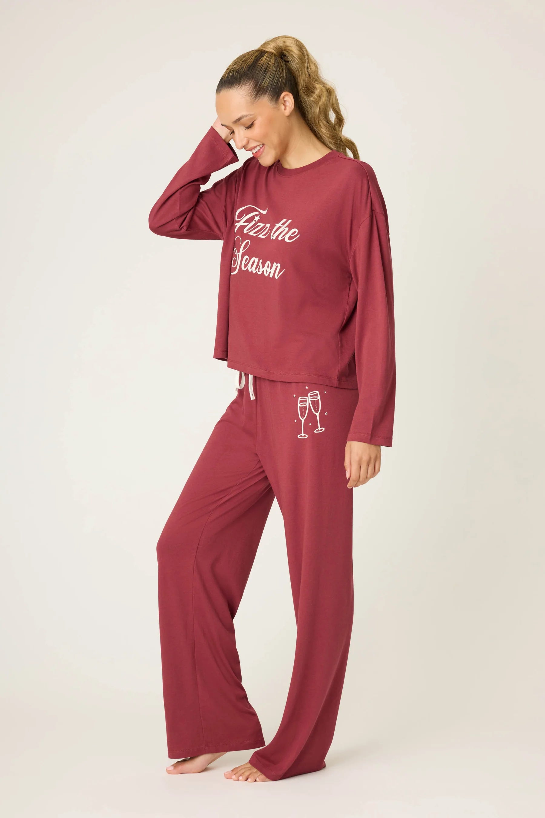 Woman wearing burgundy pajama set with 'Fizz the Season' text on a white background