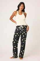 Woman wearing a white tank top and black pajama pants with cocktail pattern on a white background