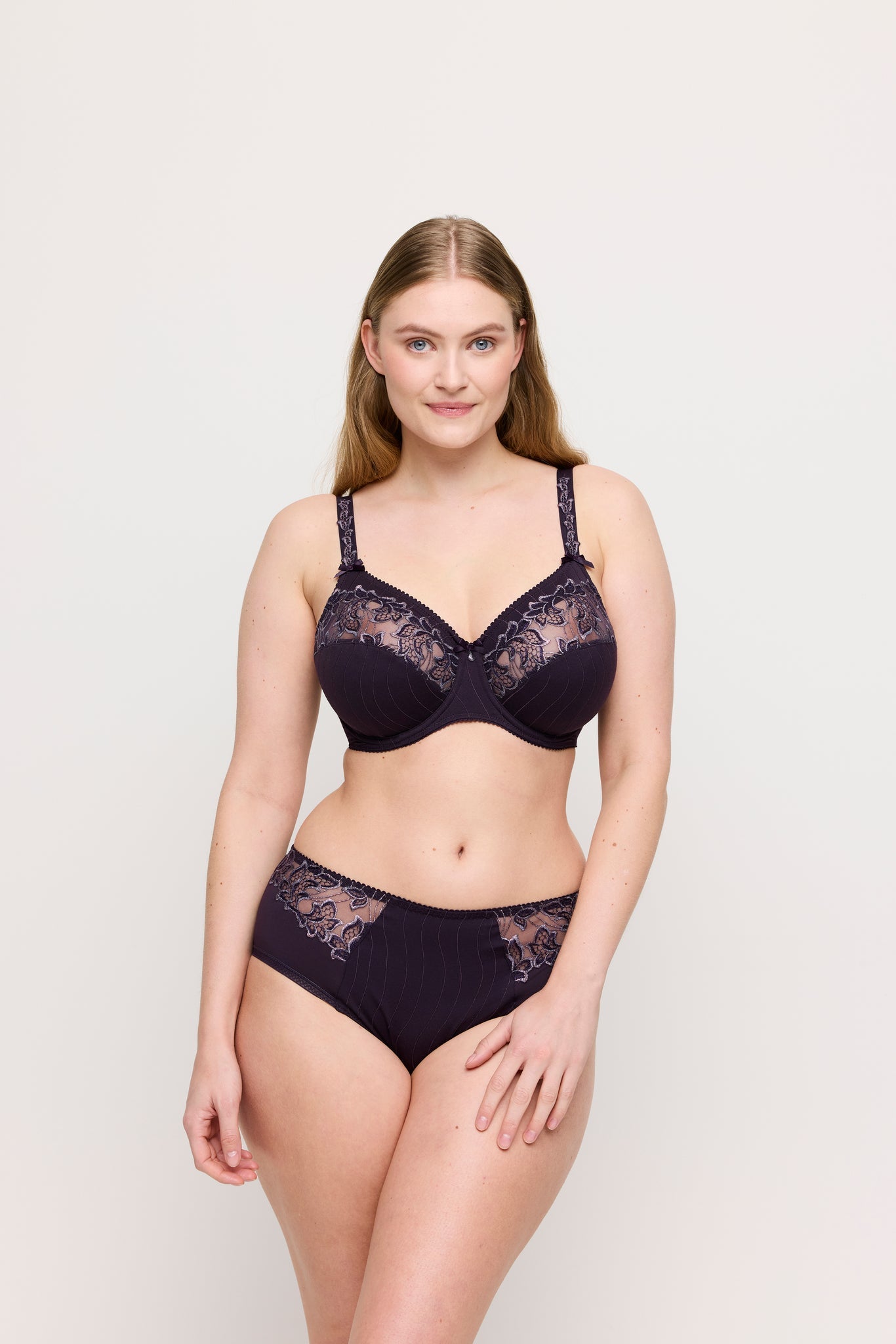 Woman wearing a dark purple lace lingerie set on a light background