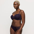 Woman wearing a dark purple bra and underwear set on a plain background