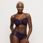 Woman wearing a dark purple bra and underwear set on a plain background