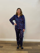 Person wearing a blue polka dot pajama set standing in a room with a white wall and wooden floor.