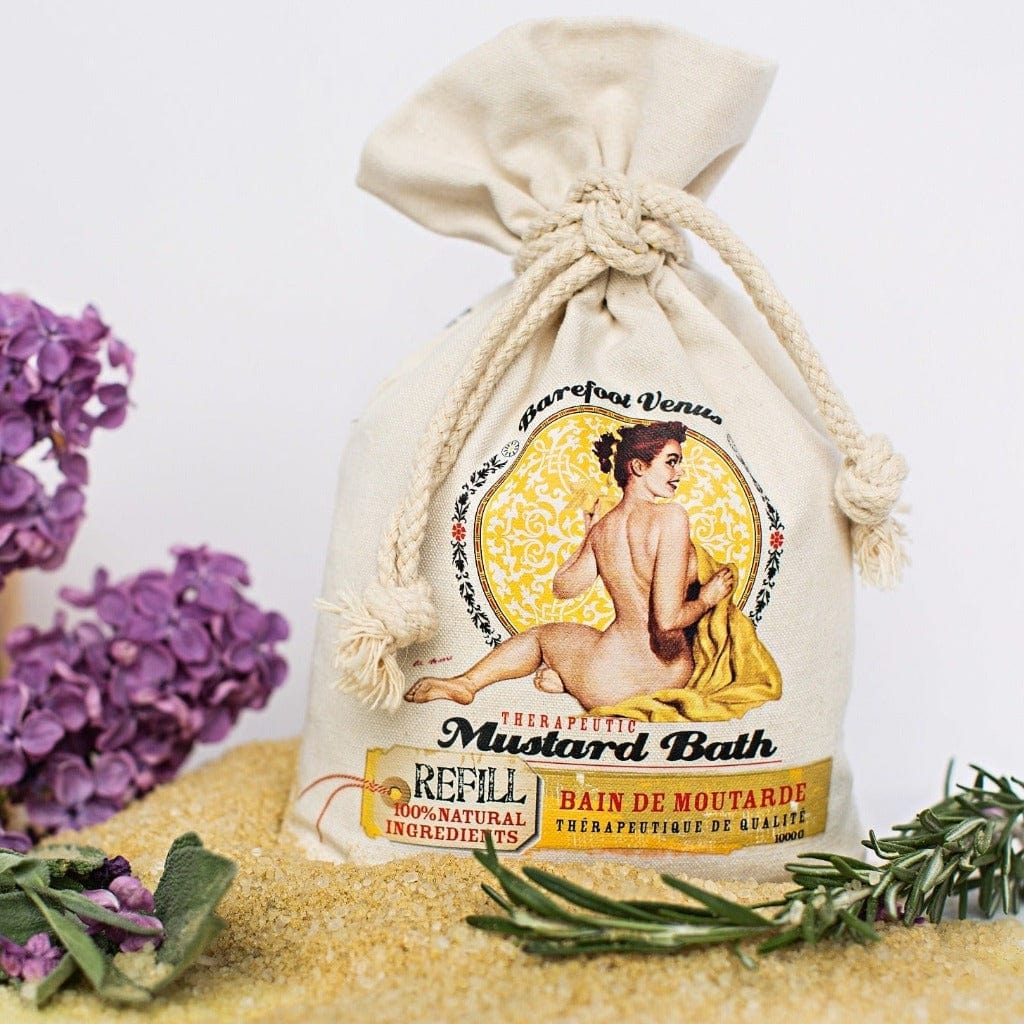 Barefoot Venus 100% Natural Mustard Bath Soak in a Canvas Bag with rope closure against a white background, with purple flowers and some of the salt around the base. 