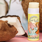Barefoot Venus Lip Bliss lip balm tube in Coconut Kiss against a coconut background. 