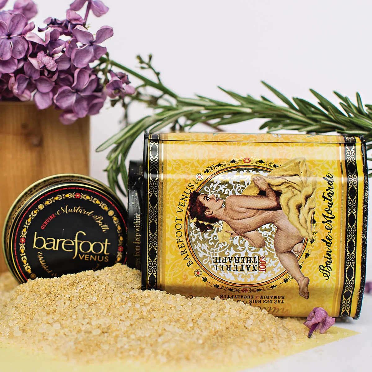 Barefoot Venus Mustard Bath in Yellow Tin container, shown against a white background, tipped on its side with some loose yellow bath salt around the base. 