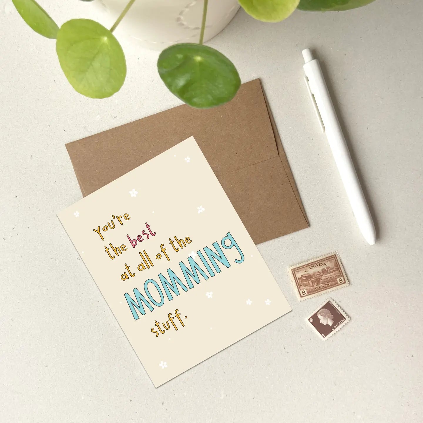 Greeting card against a beige background with a pen and envelope and stamps. 