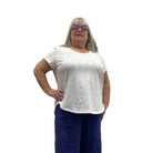 Woman wearing the Escape Cuff Sleeve Hi-Lo White T-shirt paired with navy pants against a white background. 