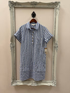 Folded blue and white striped shirt dress on a decorative silver frame against a beige wall.
