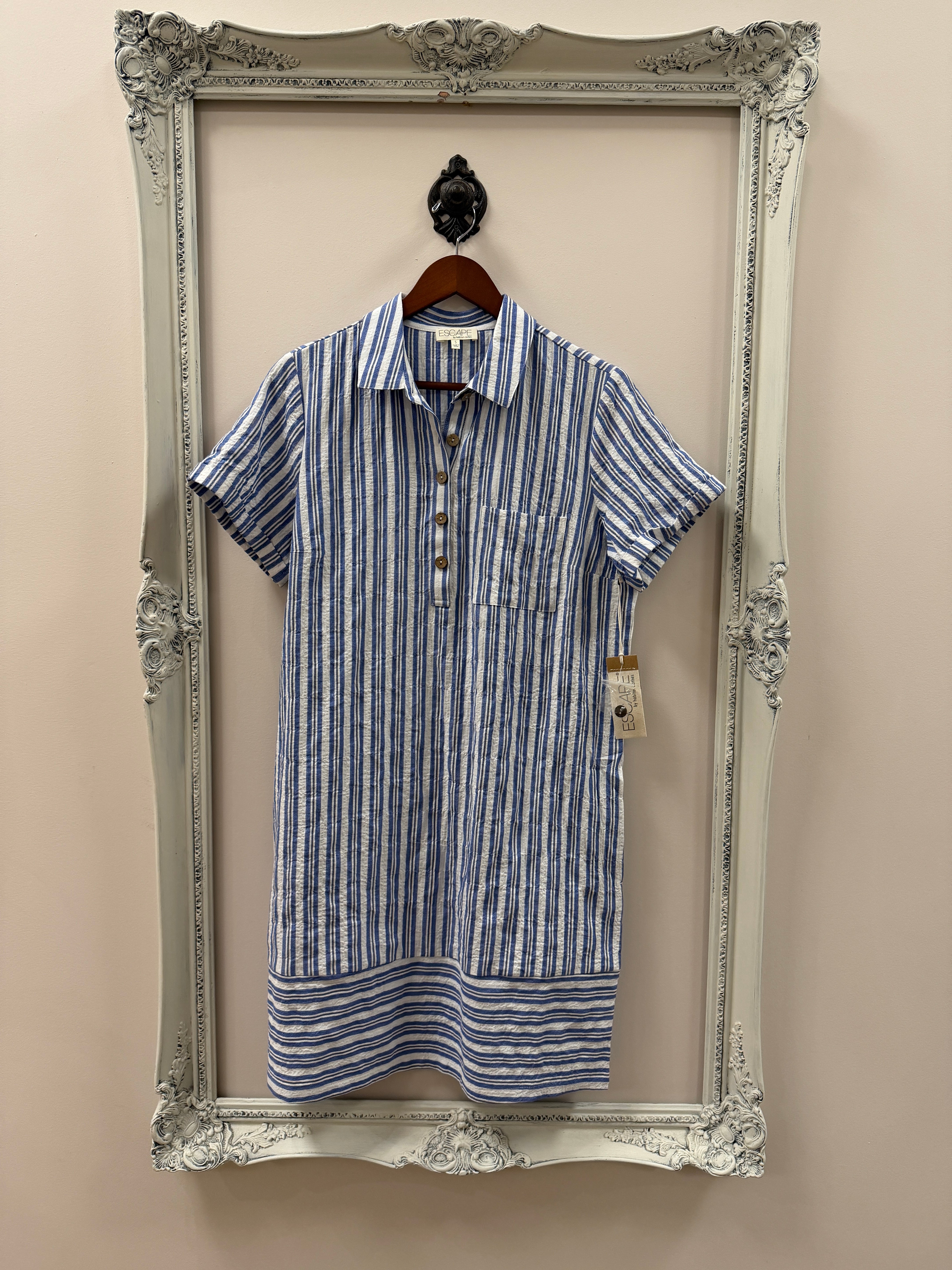 Folded blue and white striped shirt dress on a decorative silver frame against a beige wall.