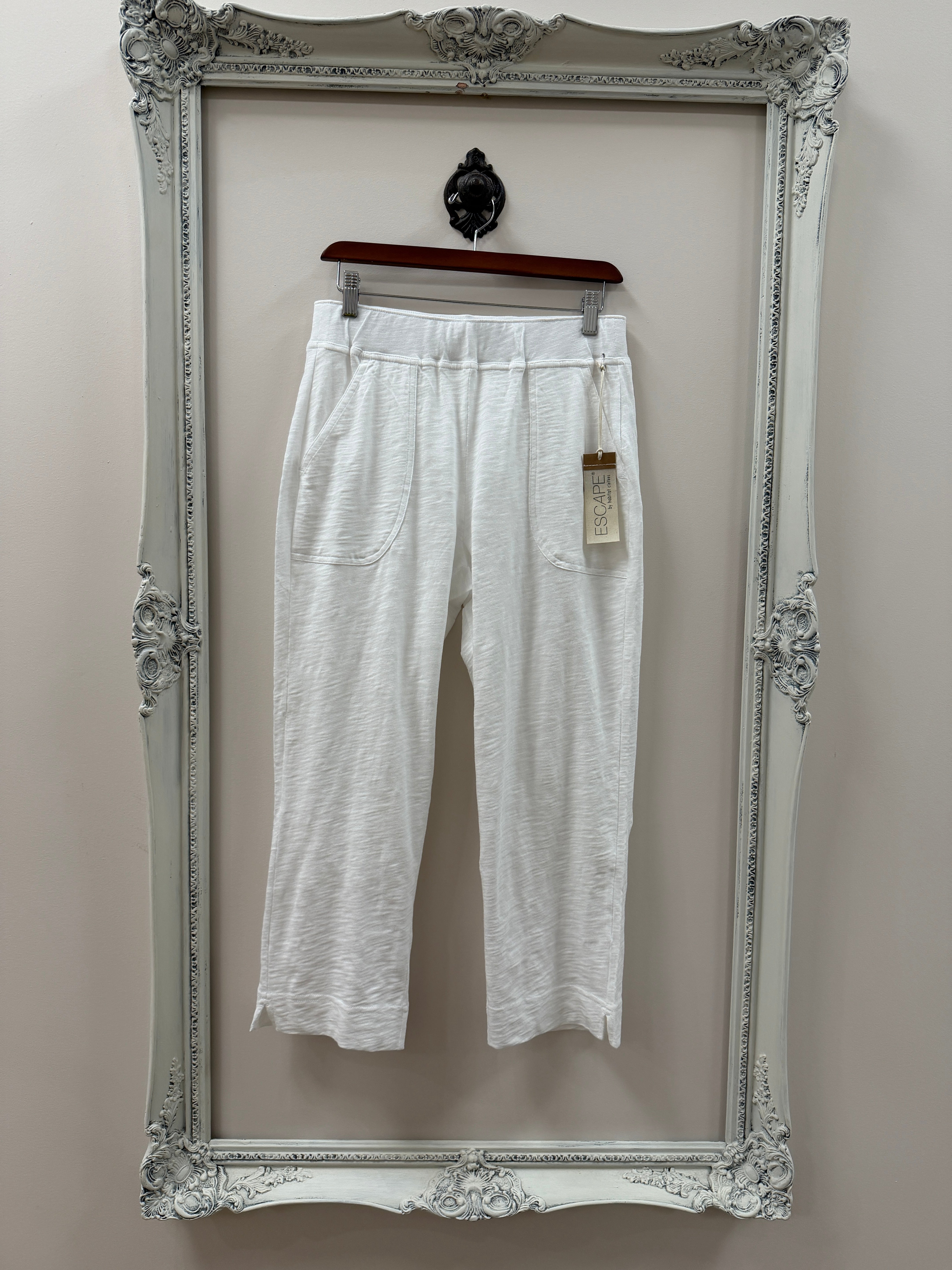 White pants on a hanger inside an ornate silver frame against a plain wall.