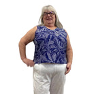 Woman wearing the blue and white floral Escape Resort tank against a white background, paired with white pants. 