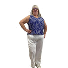 Woman wearing the blue and white floral Escape Resort tank against a white background, paired with white pants. 