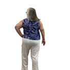 Woman wearing the blue and white floral Escape Resort tank against a white background, paired with white pants. 