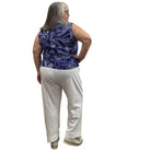 Woman wearing the blue and white floral Escape Resort tank against a white background, paired with white pants. 