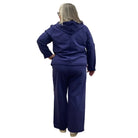Woman wearing a navy zip up Escape Solstice Hoodie over a pink shirt and with navy pants on a white background. 